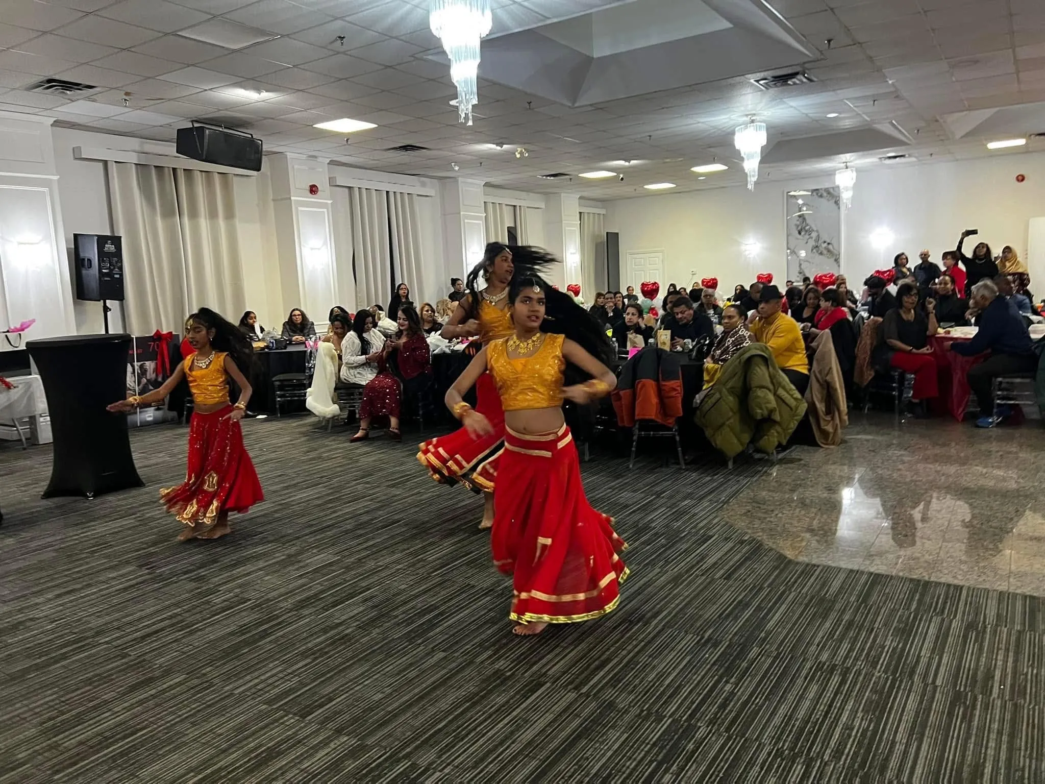 Dancers in red and gold performing in front of a full banquet hall