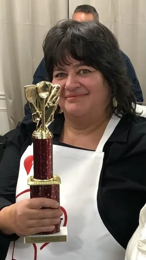 The 2025 1st place winner smiling with her trophy, wearing a One Love apron