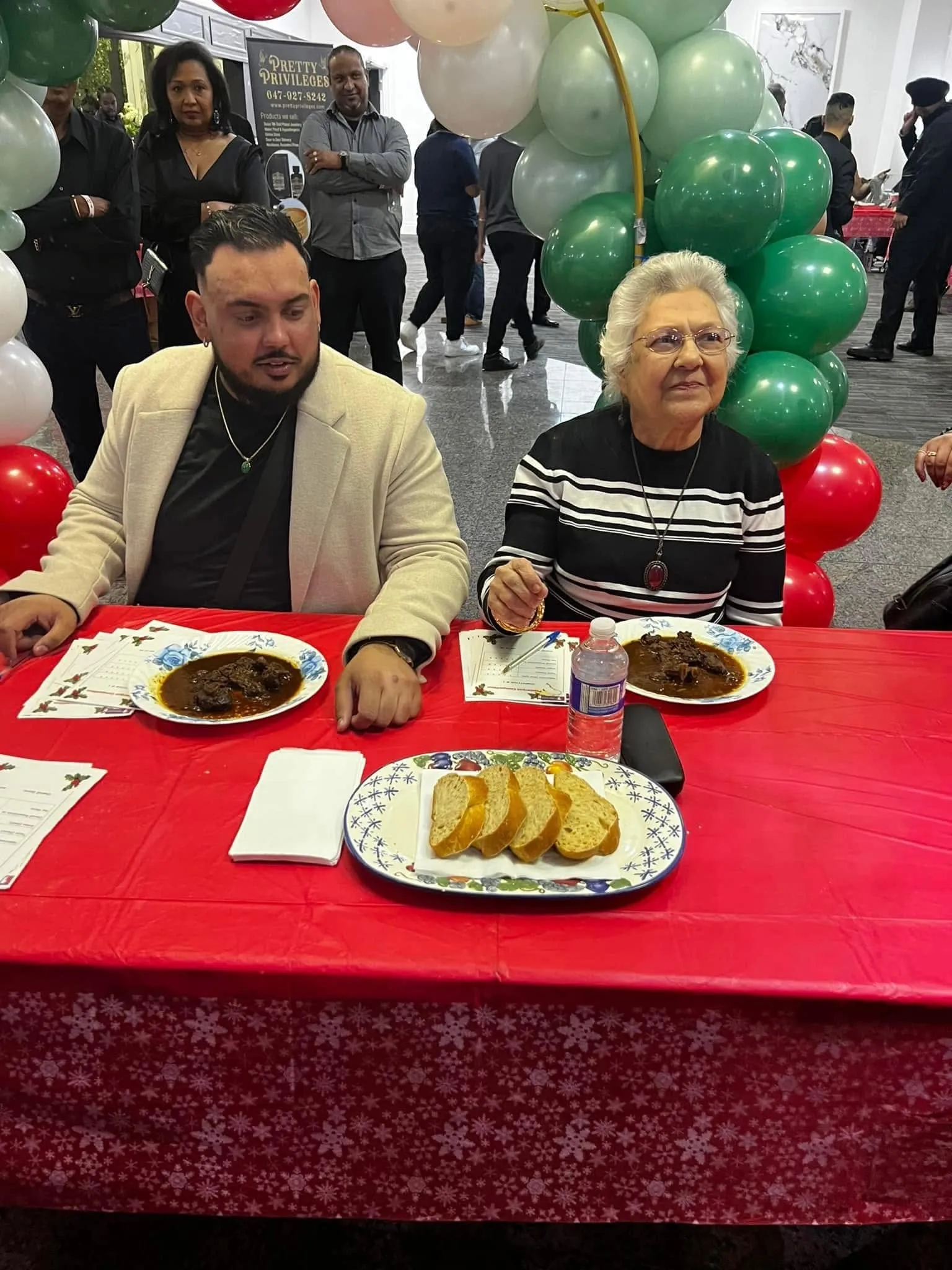 Two judges at a red table tasting plates of Pepperpot with plait bread and score sheets